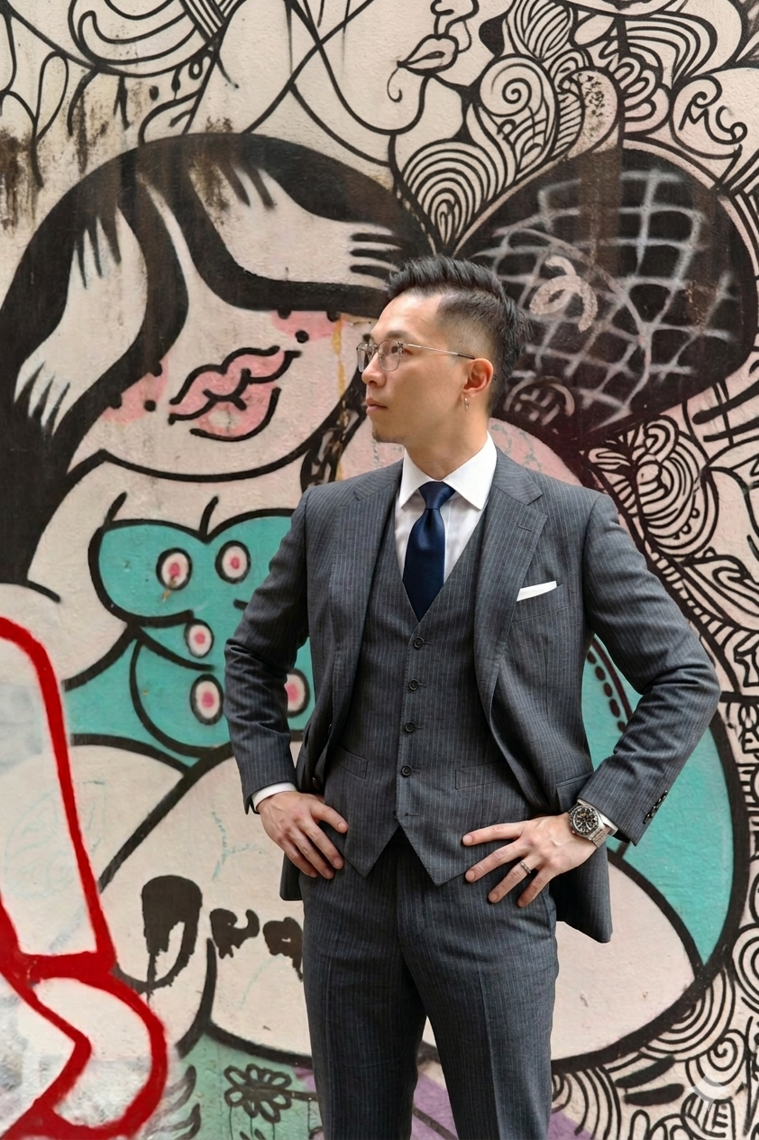 Ivor Ngo，香港增長及業務拓展負責人，身穿剪裁合身的灰色三件式西裝，站在塗鴉壁畫前。